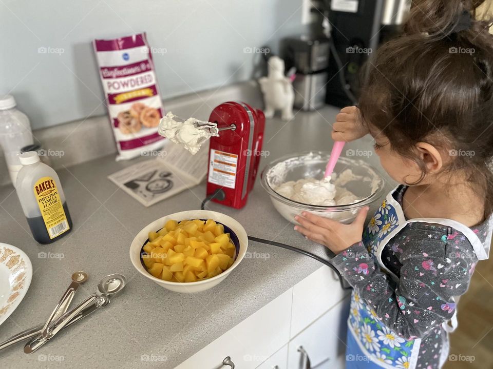 Toddler girl helps to make crepe filling, making peaches and cream crepes, making crepes at home, homemade crepes, little girl stirs whipped cream to make filling 