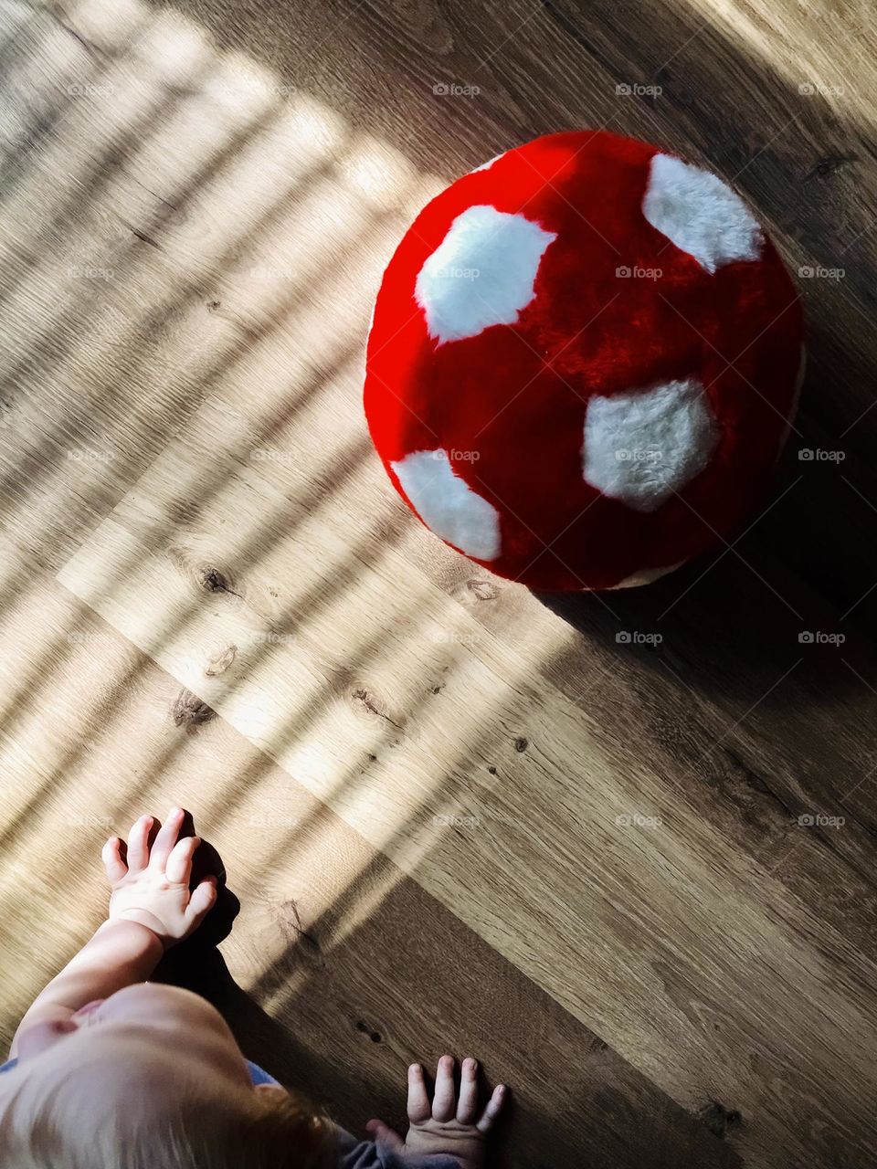 A soft red ball on the floor, light and shadow, a baby