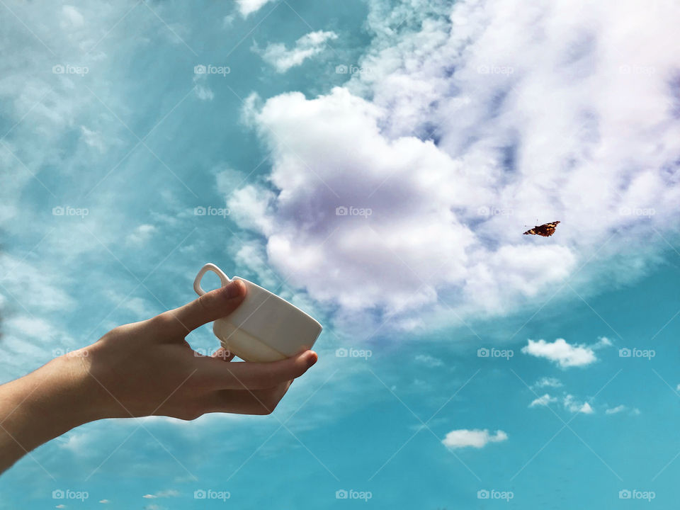 Child’s hand “catching “ white clouds into the cup from the blue sky 