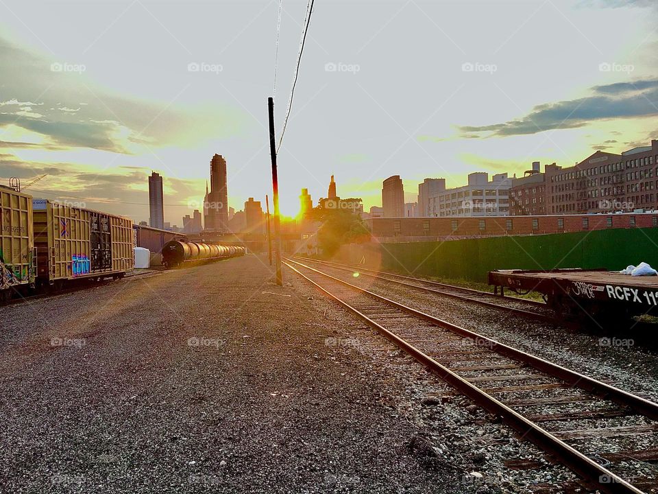 The train tracks running parallel to Borden Ave passing by the Pulaski Bridge in Long Island City, Queens, NY photographed at dusk which the sun sets and illuminates everything with a warm golden glow. 2021. Hypnotic Productions