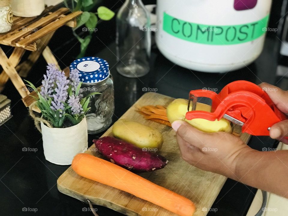 Using homemade compost for plants helps environment clean by doing daily segregation of vegetable waste . Here some root vegetables pealed out with a peeler in hands and some reusable glass containers and eco friendly  pots and compost box around it 