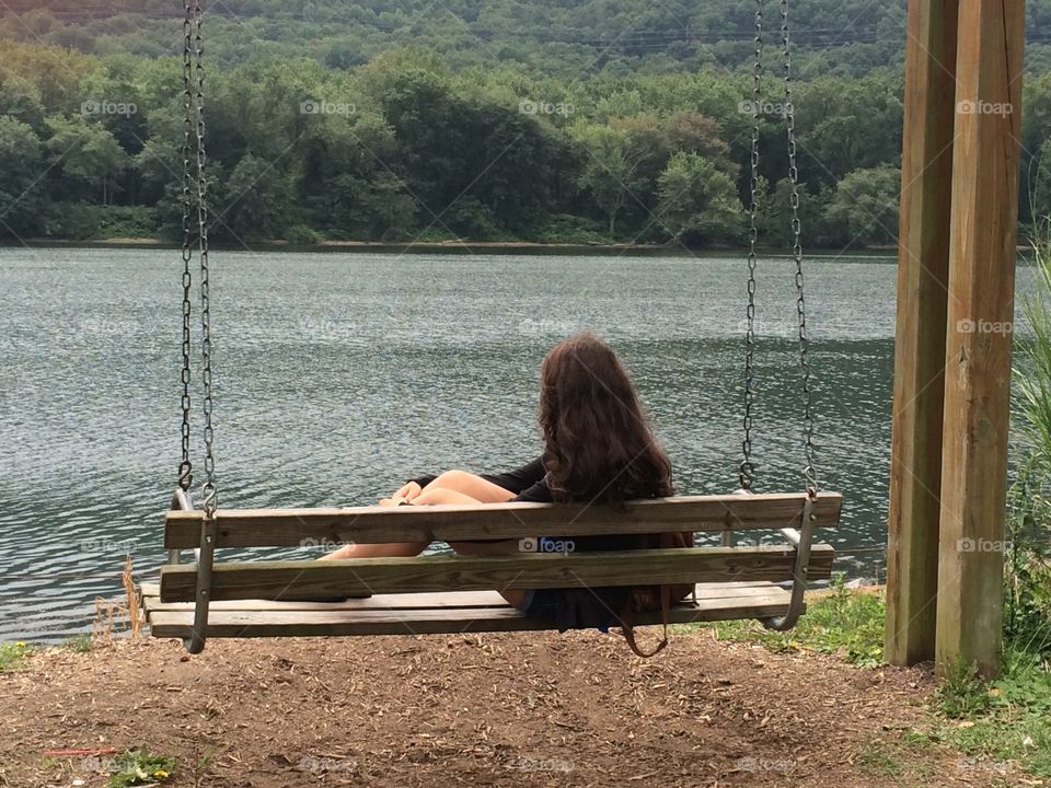 Girl reclining on swing looking at river