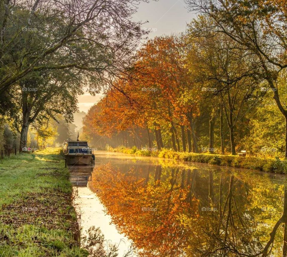A lonely barge on Malestroit canal whose banks and trees reflecting in the waters are adorned with all the colours of autumn