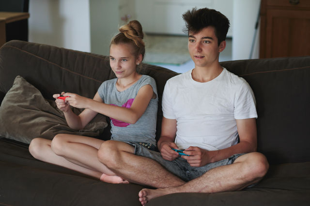 Concentrated young boy and girl playing video games sitting on sofa at home