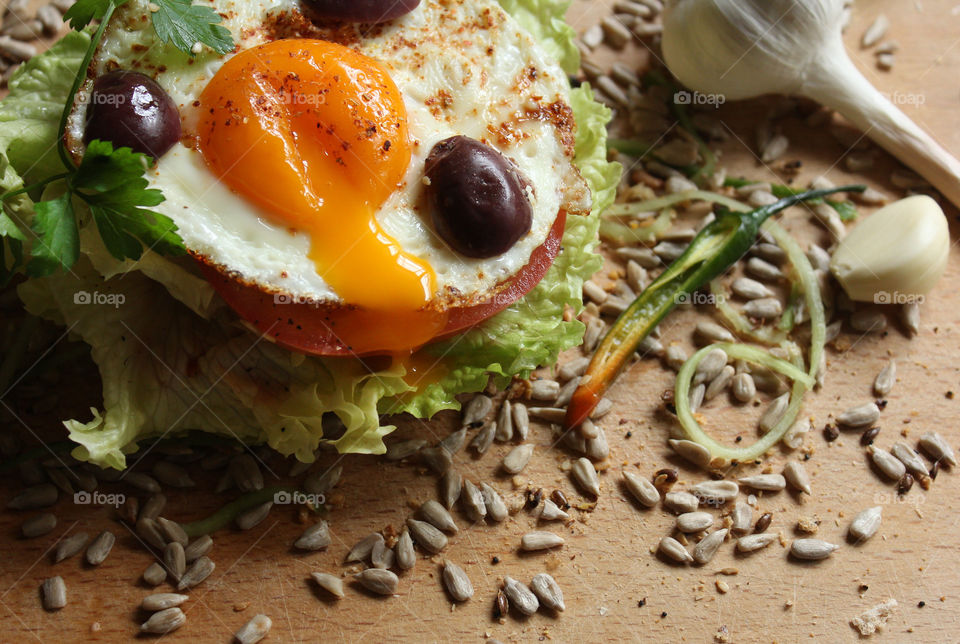 Tasty burger with fried egg, yolk, olives, lettuce, seeds, chili pepper and garlic