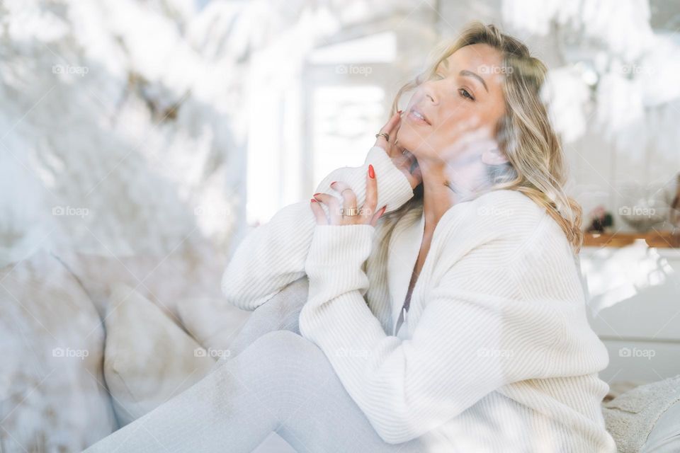 Young woman in white cardigan looking at window with winter landscape at home