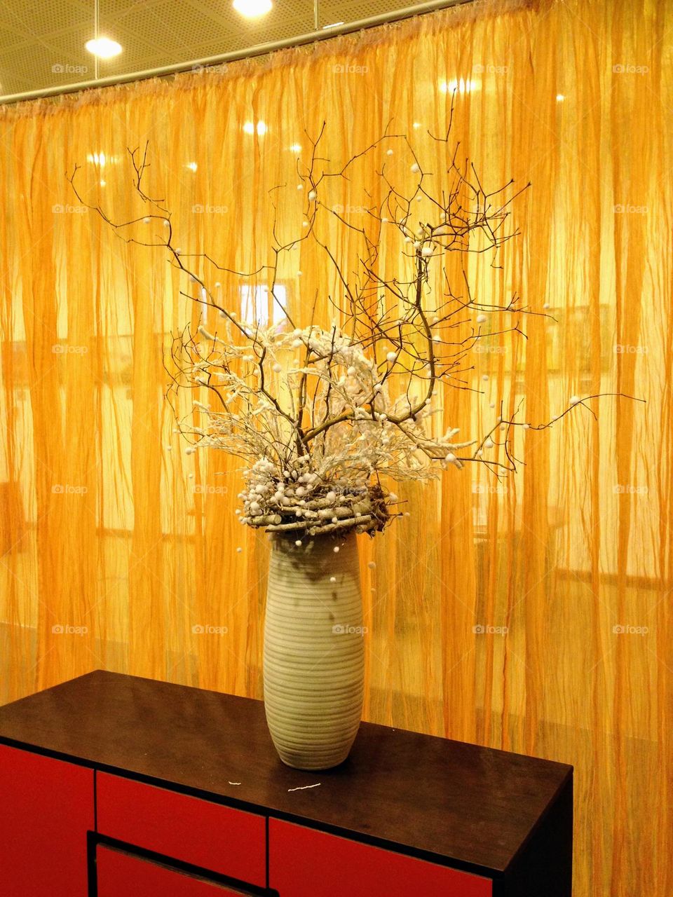 Beautiful ikebana with bizarre shape bare branches in the vase against bright yellow orange curtains 