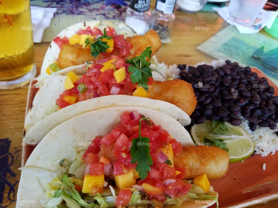 fish tacos on flour tortilla topped with mango salsa with a side of black beans and rice.
