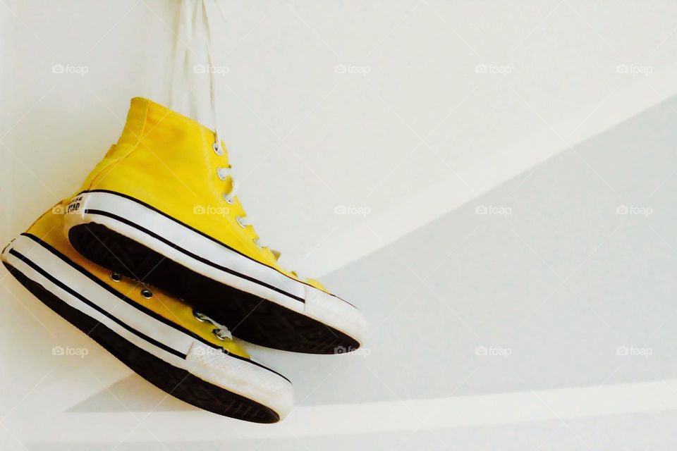 Pair of yellow sneakers hanging on the gray wall