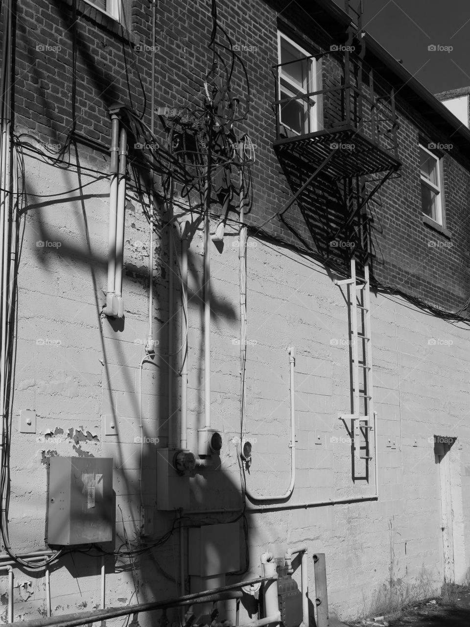 The side of an old concrete building in a city with windows and a fire escape ladder on a sunny summer day. 