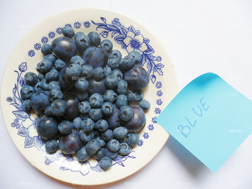 Berries of blueberries and plums on a white plate