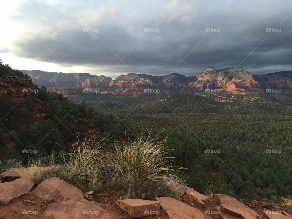 A cloudy day on a hiking trail in Sedona, Arizona near Devil's Bridge. Pictured are red Rock formations and a valley of green pine trees.