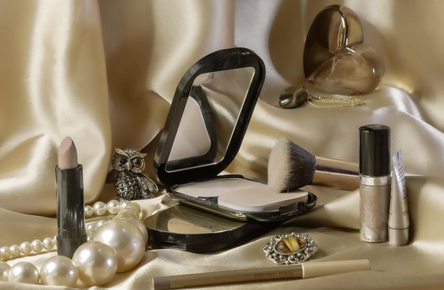 Assorted cosmetics in neutral tones, which jewellery and perfume against a silky golden background 