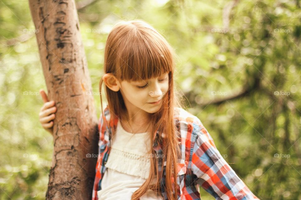 Little girl sitting on a tree with dandelion umbrellas in long hair