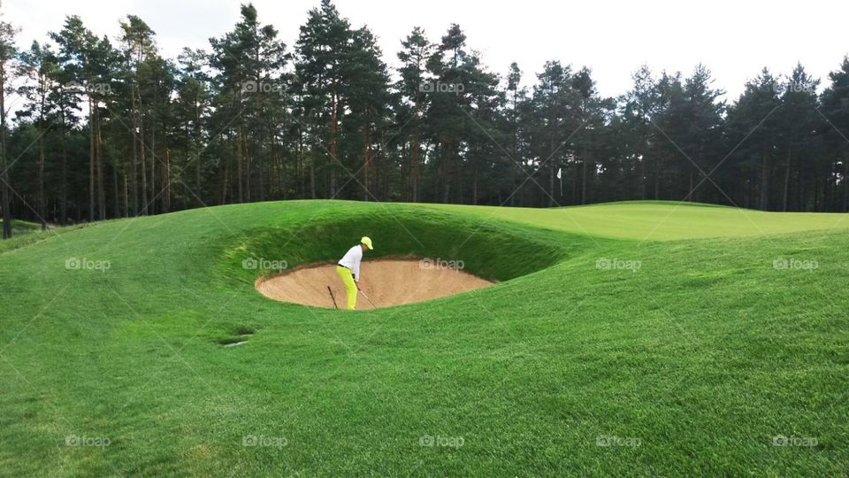A beautiful view on golf player playing from the bunker, green and trees behind