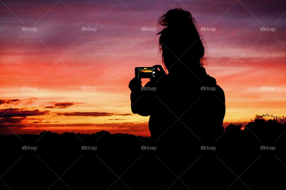 A young woman photographs a beautiful sunset with a smartphone. 