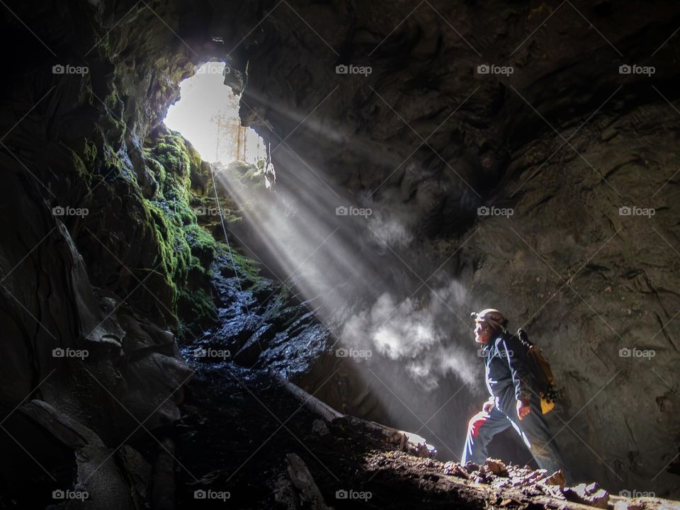 Speleologist in Sun rays at the bottom of a pit 