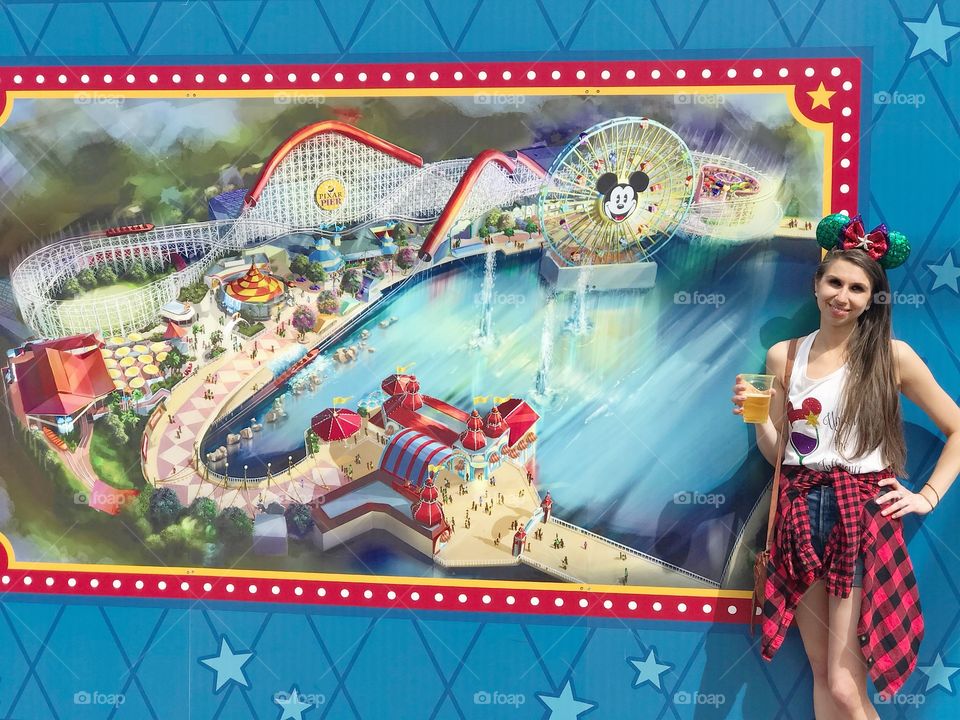 Woman standing in front of Disneyland map holding beer and wearing Mickey house ears 