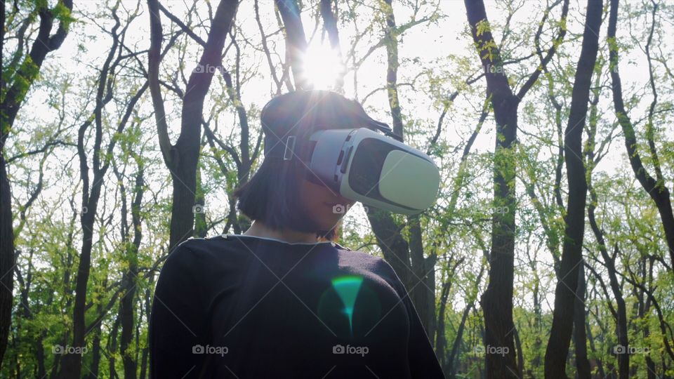 Portrait of trendy woman in casual clothing using virtual reality glasses simulator in the park or forest at spring 