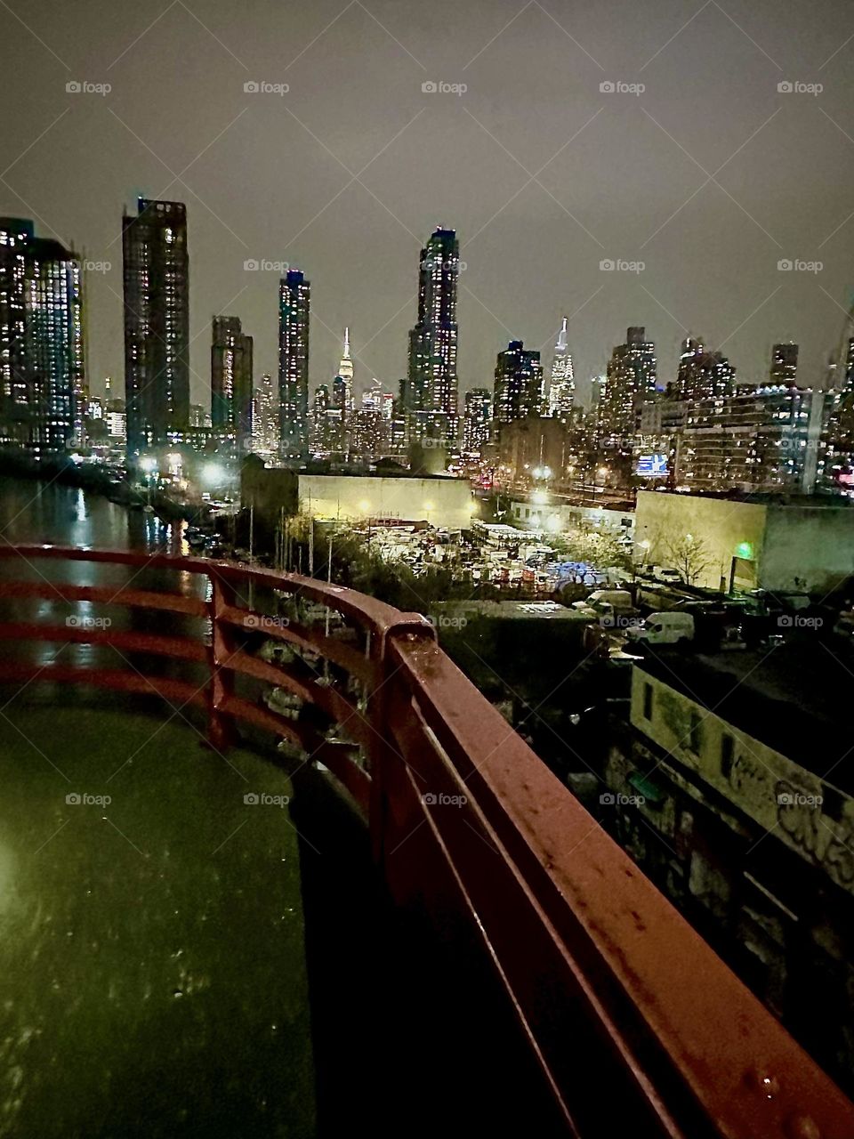 This is a nighttime view of “Newtown Creek” from the “Pulaski Bridge” that connects “Greenpoint”, Bklyn and LIC, Queens on an evening in early December 2023. The “Empire State” and the “Kreisler Bldg” in “Manhattan” are visible. Hypnotic Productions
