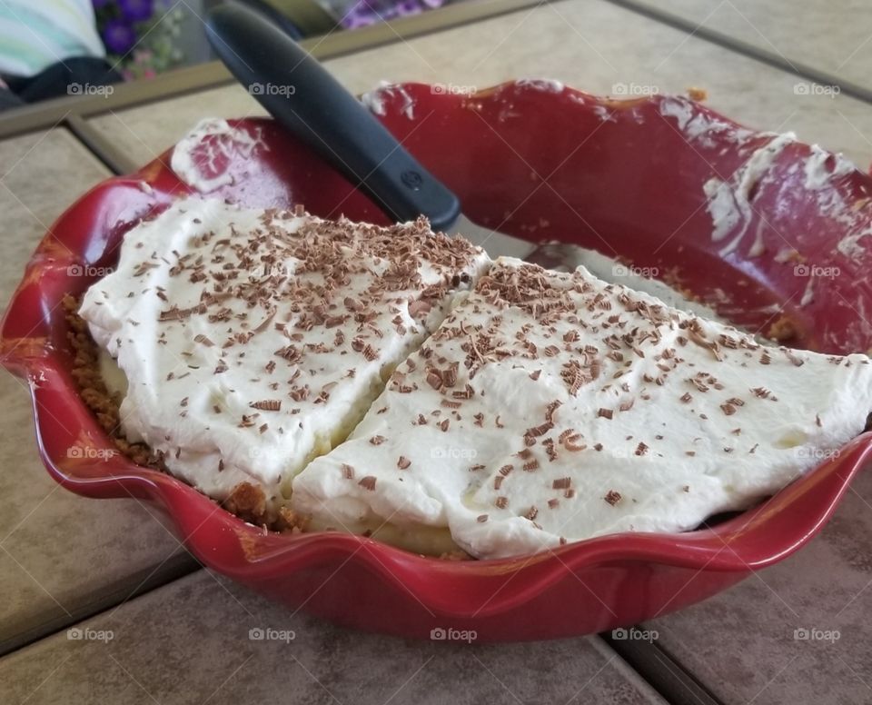 delicious banana cream pie served in a red pie dish with chocolate shavings on top.