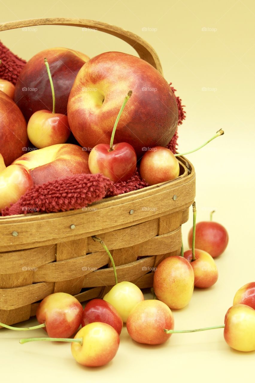 Fruits! - Nectarines And Rainer cherries in a wooden basket against a yellow background 