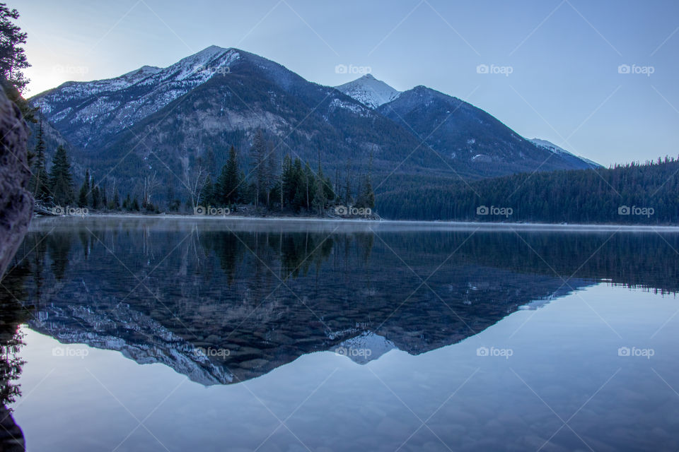 A mirror like reflection of snowy mountain peaks on a cool montana lake at sunrise. 