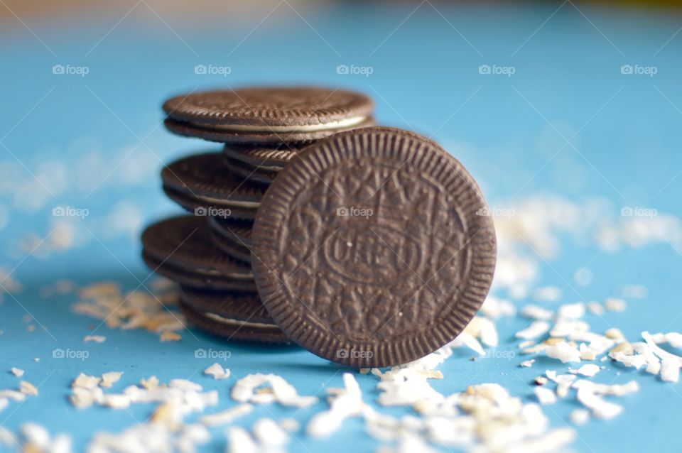 A stack of coconut Oreo thin cookies on a blue background with coconut shreds
