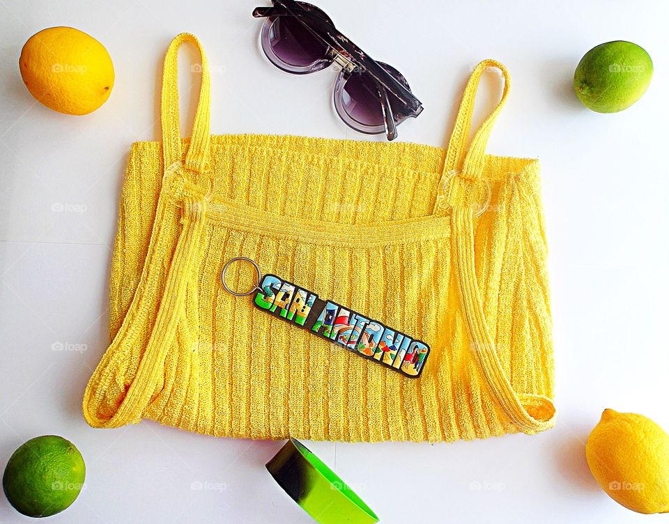 Yellow tank top with sunglasses, a bracelet, a Keychain, limes and lemons on a white background 