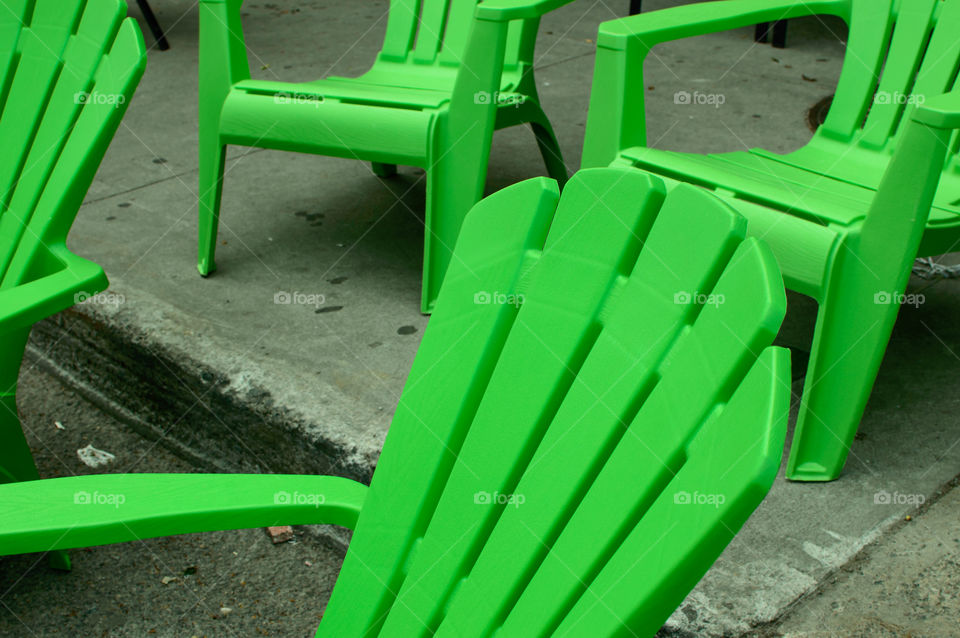 Closeup of rows of green plastic lawn chairs arranged in street on concrete ready for people to sit and relax and watch outdoor show, urban lifestyle conceptual street photography 