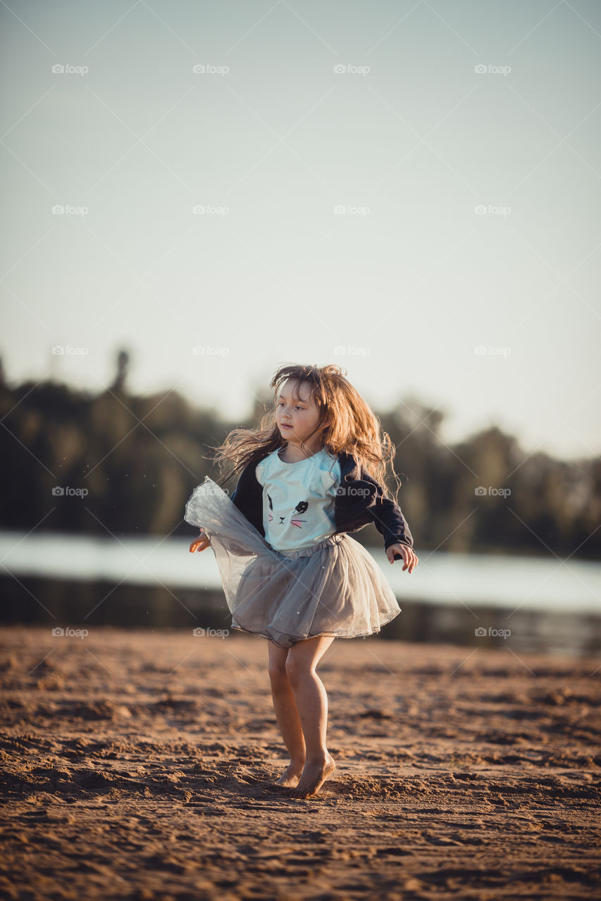 Little girl on lake coast at sunny evening. 