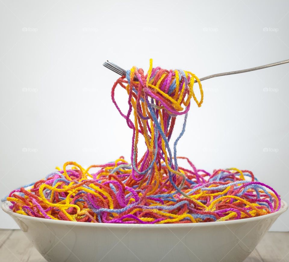 A bowl of colourful wool spaghetti twisted around a fork