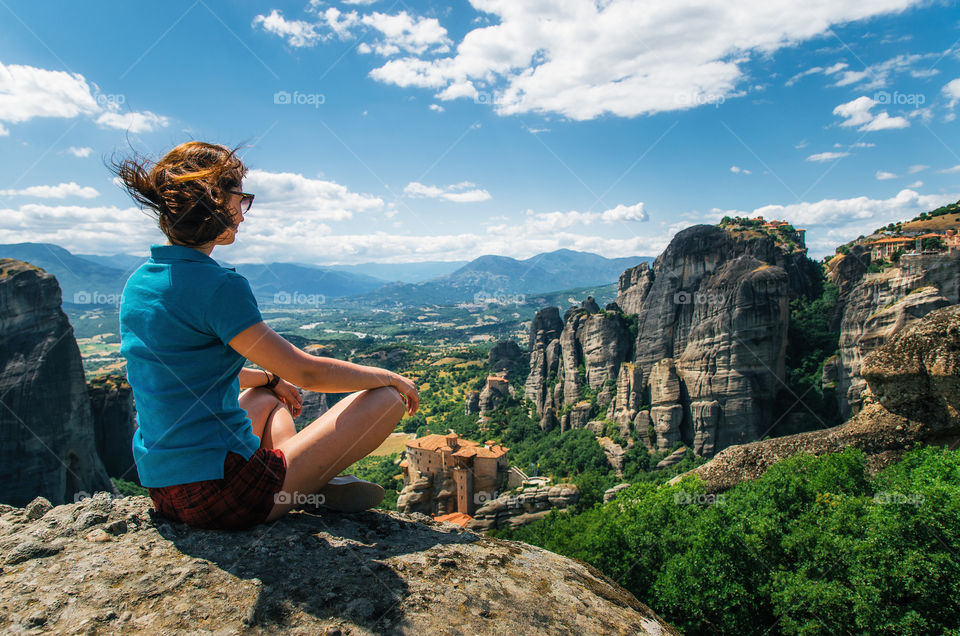 Young woman sits back to the camera on top of the mount and looks at the valley and rocks, Meteora, Greece