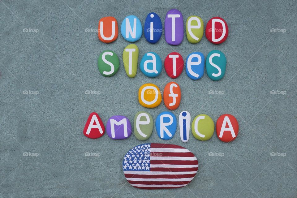 United States of America, creative text composed with multi colored stone letters and stone USA flag over green sand