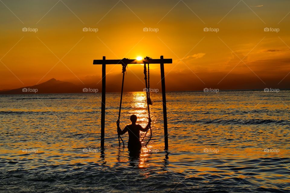 Silhouette of single woman alone swinging on the beach