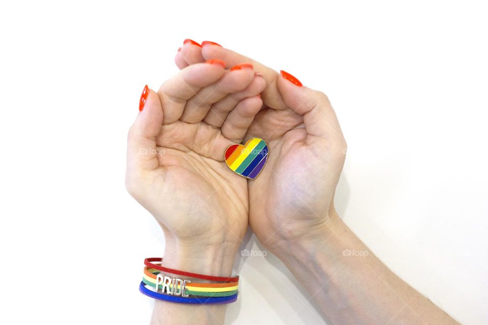 Women's hands hold a rainbow heart. Pride rainbow bracelet. LGBT love