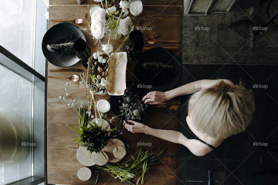 Blonde girl is serving water table with flowers and decor, shot from the above