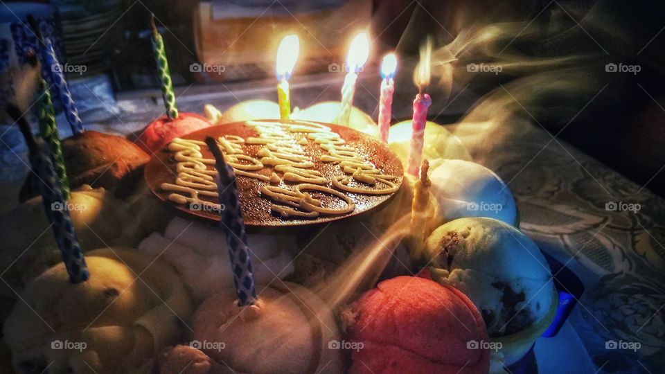 Birthday cake with candles in the process of being blown. Some candles are still lit while others have already been extinguished. In this low light image, smoke can be seen to billow in different directions.