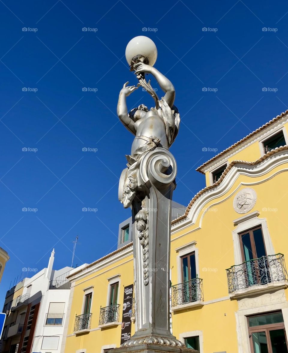 View looking up at a statue of woman holding an orb in front of an old ornate yellow building with deep blue sky in the background. 