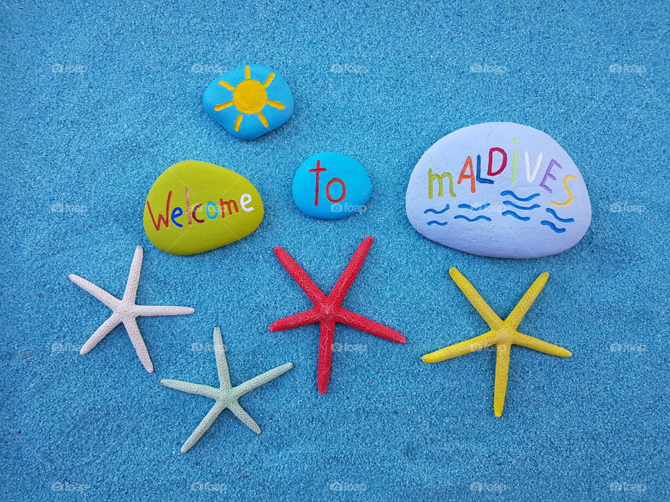 Welcome to Maldives, souvenir with starfishes and colored stones over blue sand