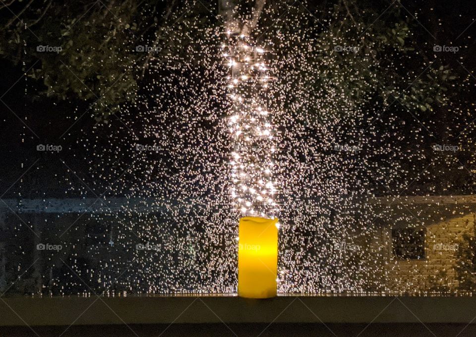 raindrops on a screen illuminated by a candle and lights wrapped around a tree trunk
