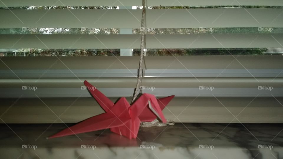 A hand made oragami crane perched on top a window sill.