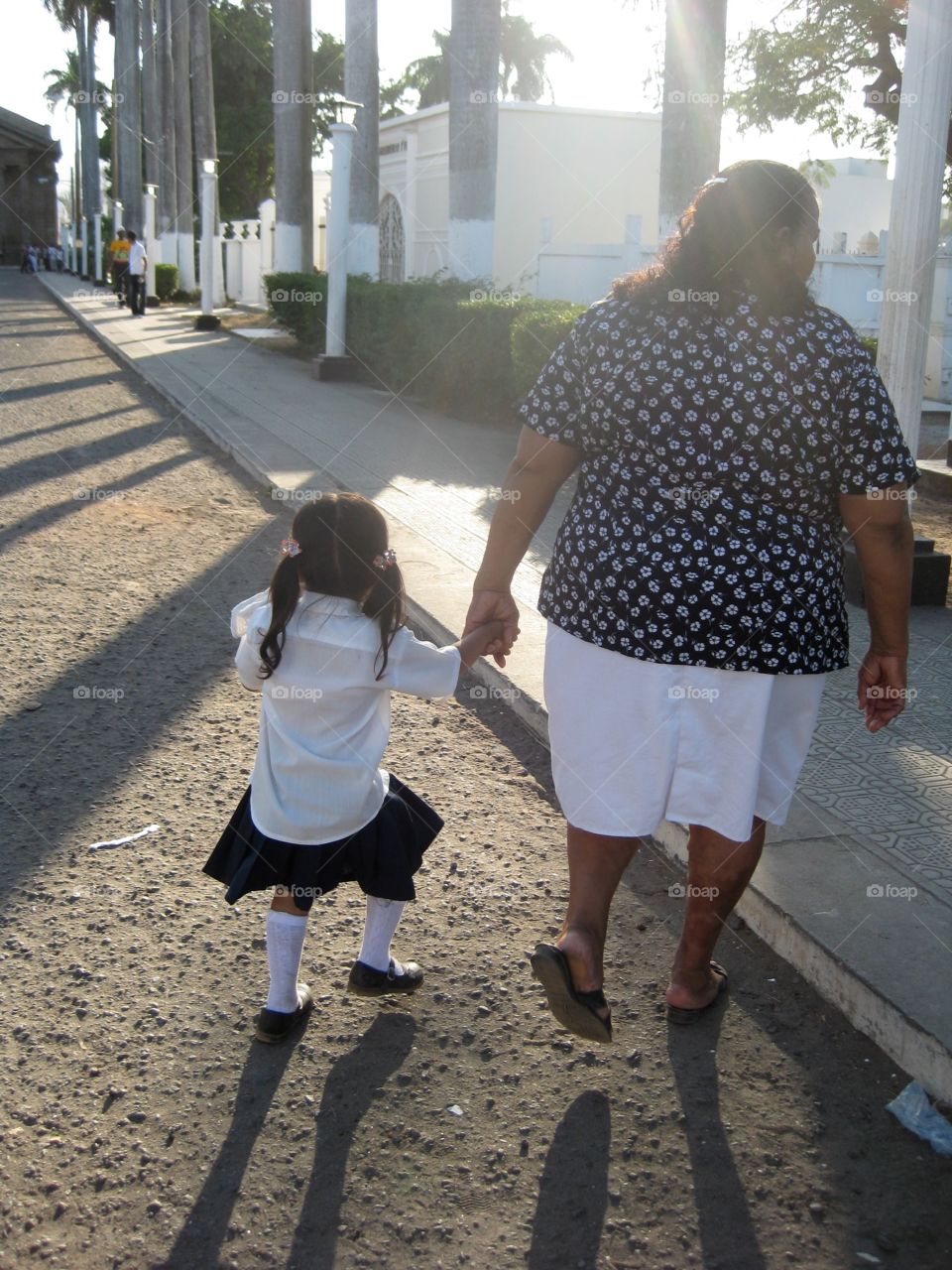 Home from school. Granada, Nicaragua. Grandma walking granddaughter home from school, passing through the cemetery 