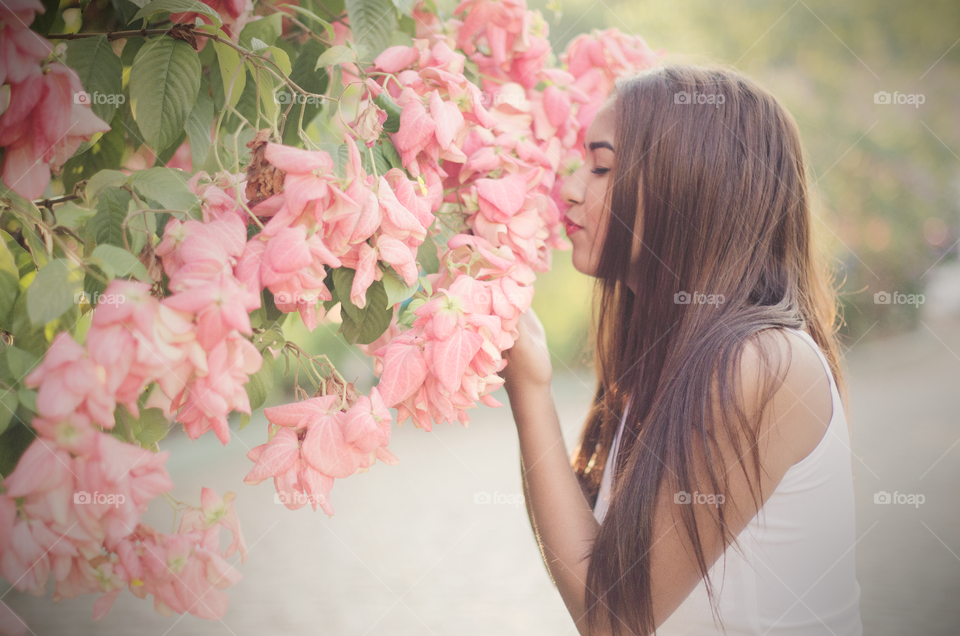 Young girl smelling pink flower in the garden