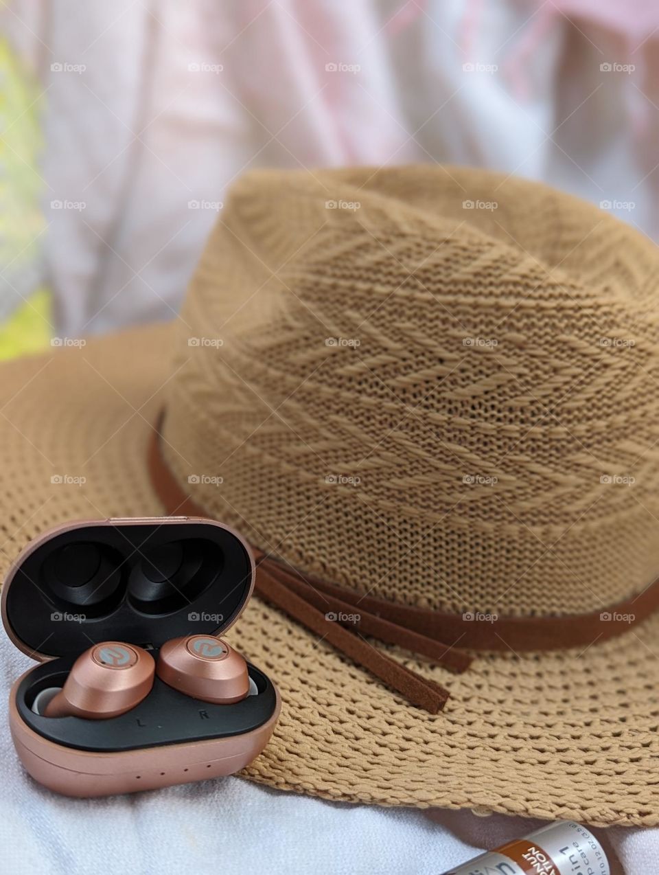 tan sun hat and rose colored ear buds essential travel items for summer beach vacation road trip vacay