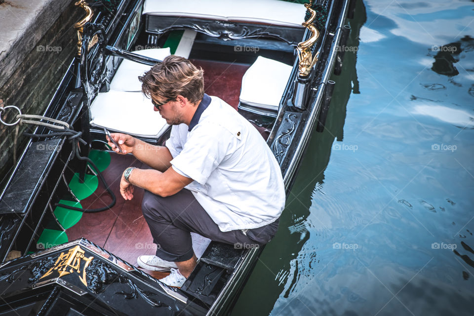 Young Gondolier Using His Smartphone Inside His Gondole
