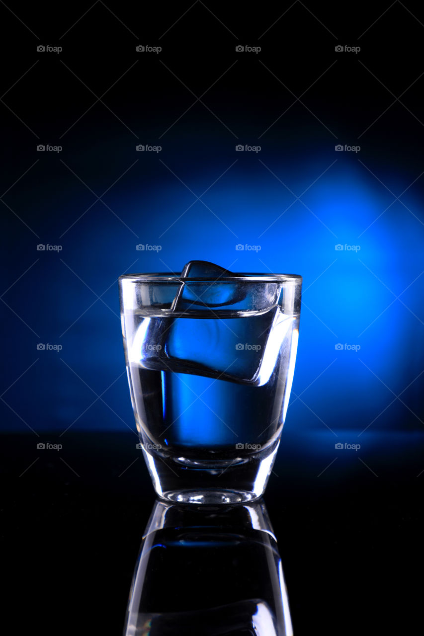 Shot glass on blue background with an ice cube