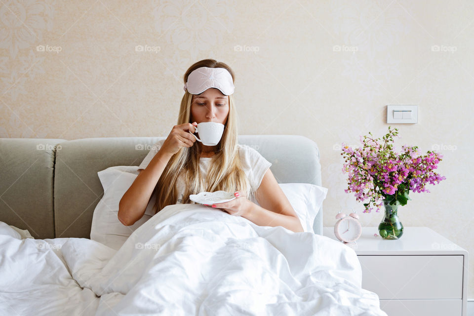 Young woman with blonde hair drinking coffee in bed