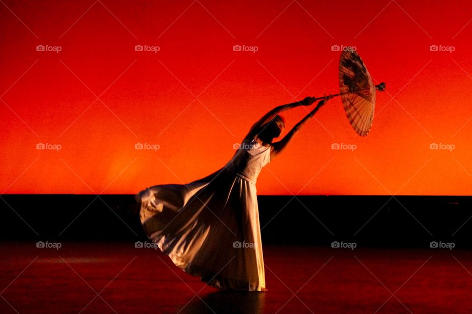 Dancer with a traditional Chinese oil-paper umbrella leans to the side in a beautiful flowy dress against a dark red dramatic background