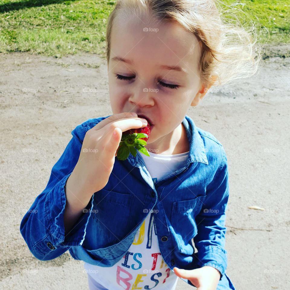 toddler eating strawberry outside